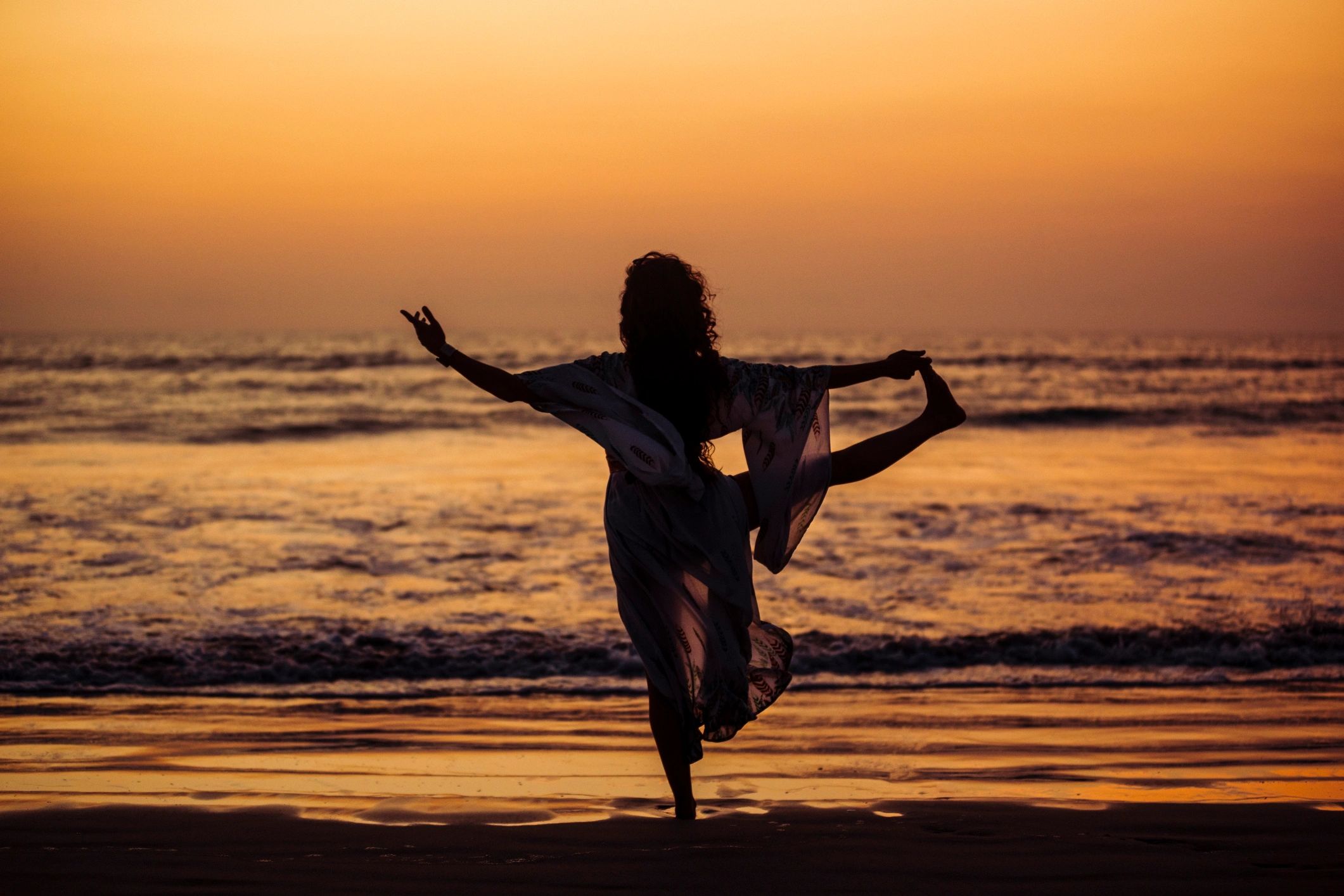 Woman practicing yoga on a beach at sunrise, facing the ocean
