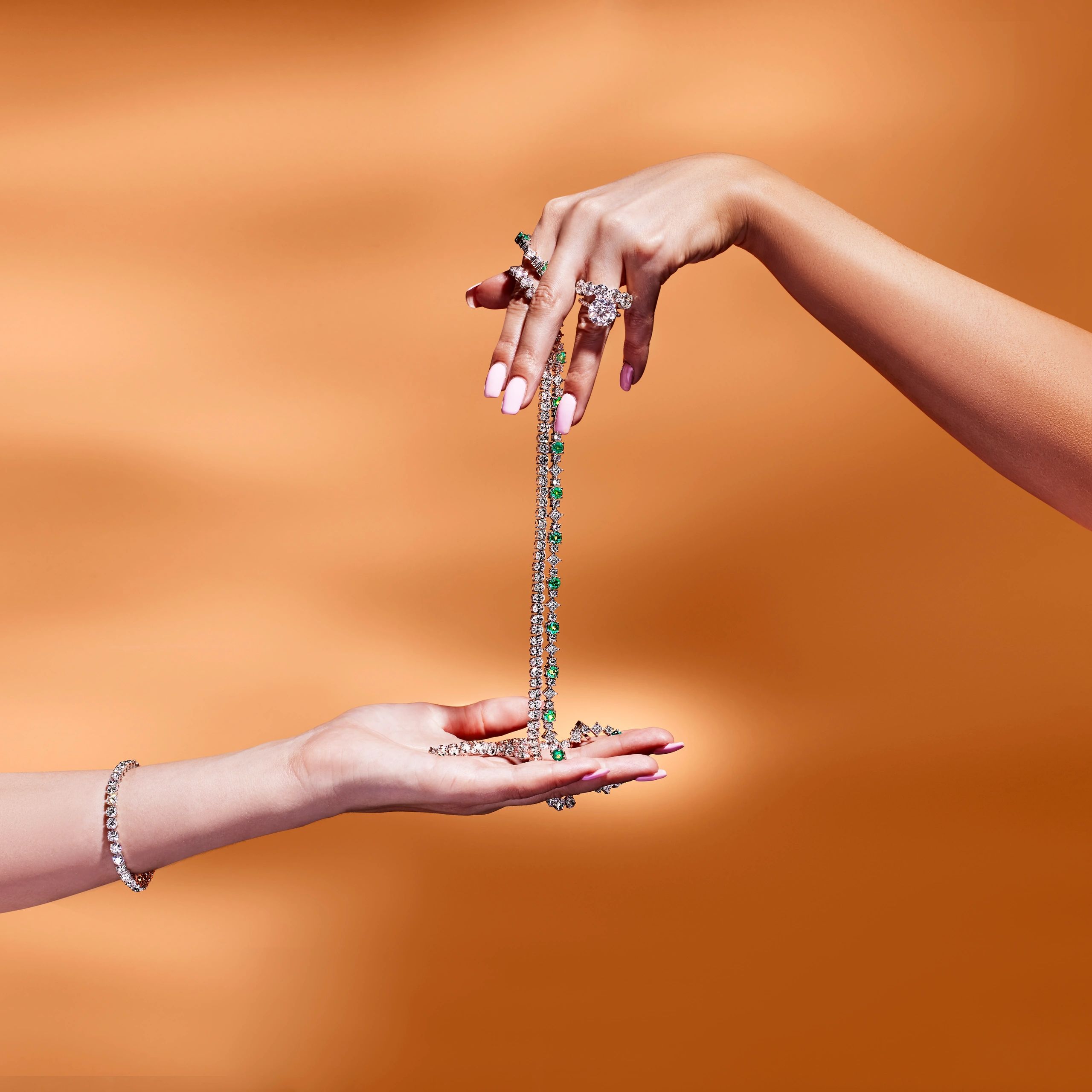 Two hands reaching toward each other holding a piece of jewelry