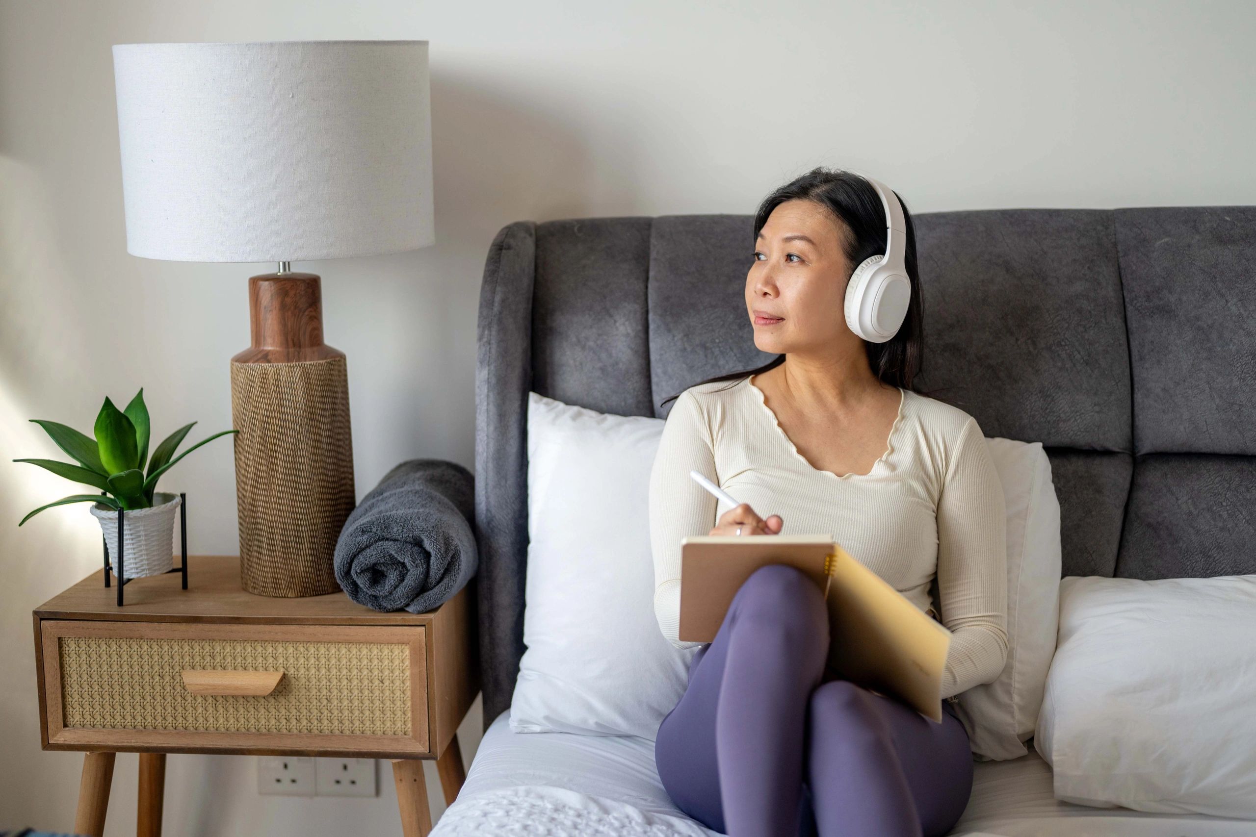 Woman writing in a diary on a bed near a window